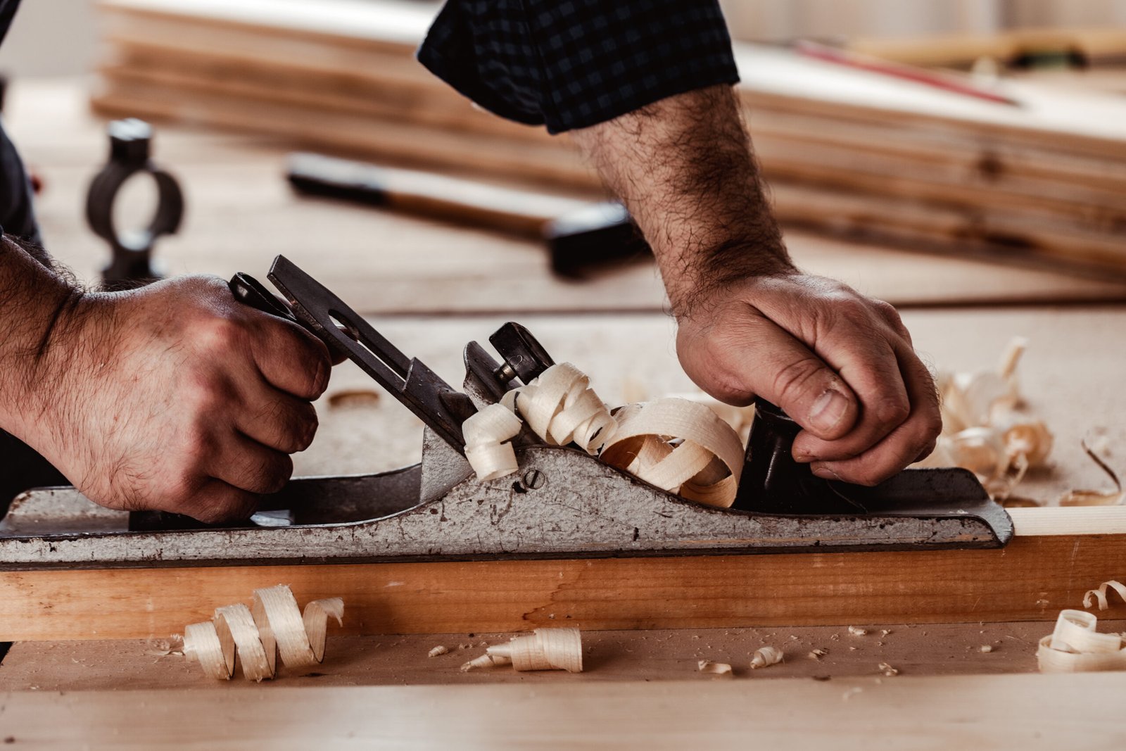 Carpenter's hands planing a plank of wood with a hand plane