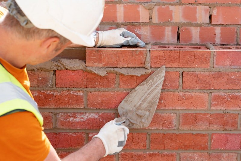 Bricklayer laying bricks on mortar on new residential house construction. Get NVQ in bricklaying